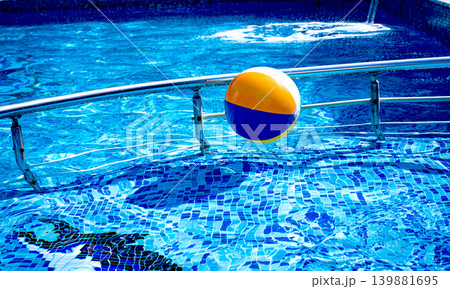 Colorful beach ball floating on the surface of a sparkling blue swimming pool during a sunny day Colorful beach ball floating on the surface of a sparkling blue swimming pool during a sunny day 139881695