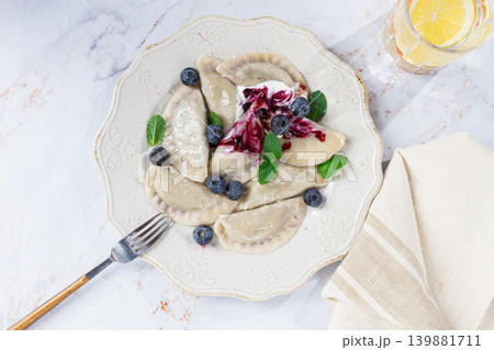 Delicious homemade dumplings served with berry sauce and fresh blueberries on a white plate 139881711