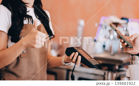 Asian senior female barista adult receiving mobile payment from customer using smartphone at cafe demonstrating modern cashless transaction in cozy local family coffee shop 139881922