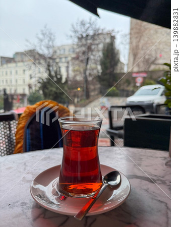 Traditional Turkish tea in tulip-shaped glass stands on cafe table near rainy street window with blurred urban background, cozy atmosphere. Hospitality branding, travel food, rainy weather, restaurant 139882831