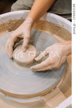 Creative sculpting. Artisan hobby. Unrecognizable female hands specialist working with raw clay pot using wheel in professional craft workspace. Creative sculpting. Artisan hobby. Unrecognizable female hands specialist working with raw clay pot using wheel in professional craft workspace. 139883186