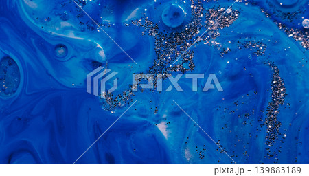 Liquid glitter flow. Shimmering art. Defocused blue color sequin bright particles floating in paint water wave on abstract background. Liquid glitter flow. Shimmering art. Defocused blue color sequin bright particles floating in paint water wave on abstract background. 139883189
