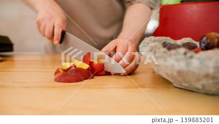 Hand cutting peach. Fruit preparation. Unrecognizable professional man chef using sharp knife on wooden board making peeling plums dessert in kitchen. Hand cutting peach. Fruit preparation. Unrecognizable professional man chef using sharp knife on wooden board making peeling plums dessert in kitchen. 139883201