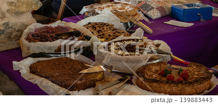 Cakes and pies are set on a table at a local market festival. Visitors walk around, looking at the variety of homemade desserts and enjoying the atmosphere of the event. Cakes and pies are set on a table at a local market festival. Visitors walk around, looking at the variety of homemade desserts and enjoying the atmosphere of the event. 139883443