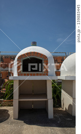 This outdoor wood fired brick oven sits on a concrete stand. It has a white dome shape and is placed outside under a clear blue sky. Perfect for cooking various dishes. This outdoor wood fired brick oven sits on a concrete stand. It has a white dome shape and is placed outside under a clear blue sky. Perfect for cooking various dishes. 139883445