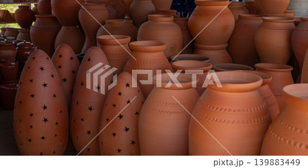 Visitors explore a rustic market shop filled with traditional terracotta clay pots and handmade ceramic lantern cones. The shop showcases local craft and culture. Visitors explore a rustic market shop filled with traditional terracotta clay pots and handmade ceramic lantern cones. The shop showcases local craft and culture. 139883449