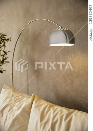 Close-up of chrome arc floor lamp illuminating white pillows in grey loft interior	 139883467
