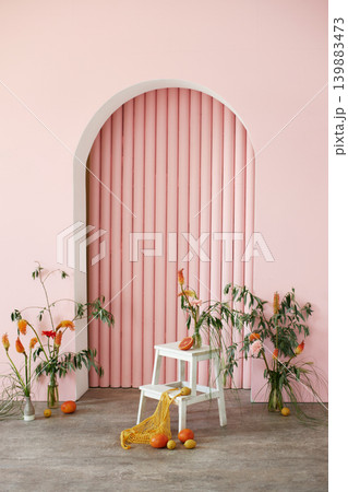 Creative pink studio interior with arch, white ladder, exotic flowers, and citrus fruits Creative pink studio interior with arch, white ladder, exotic flowers, and citrus fruits 139883473