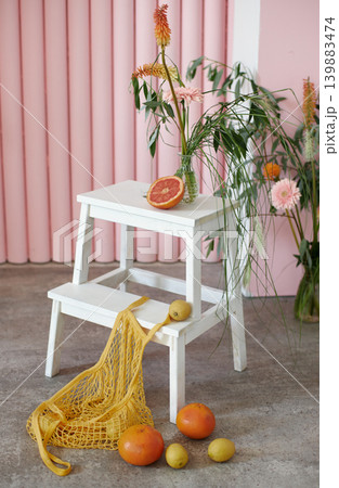 Close-up of white wooden ladder with fresh grapefruits, lemons, and yellow mesh bag on pink background	 139883474