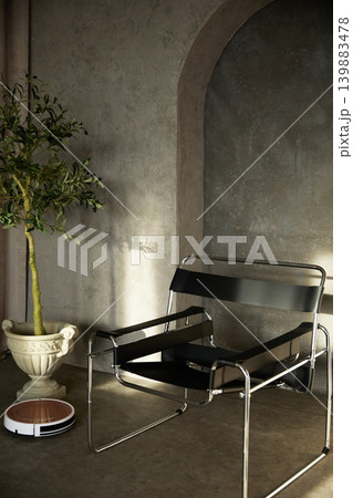 Modern black leather armchair and robot vacuum cleaner in concrete loft interior with olive tree 139883478