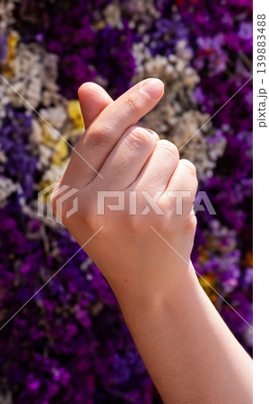 Hand making a finger heart gesture against a colorful floral background 139883488