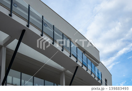 The structure displays minimalistic design with large glass balconies and strong black metal pillars. The view is taken from below, highlighting the cloudy sky above the modern architecture. The structure displays minimalistic design with large glass balconies and strong black metal pillars. The view is taken from below, highlighting the cloudy sky above the modern architecture. 139883493