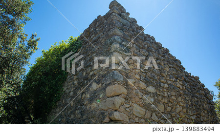 View shows a stone structure covered in ivy at the Atzuvieta archaeological site. The sunlight shines on the historic stones. Nature surrounds the ancient site. View shows a stone structure covered in ivy at the Atzuvieta archaeological site. The sunlight shines on the historic stones. Nature surrounds the ancient site. 139883494