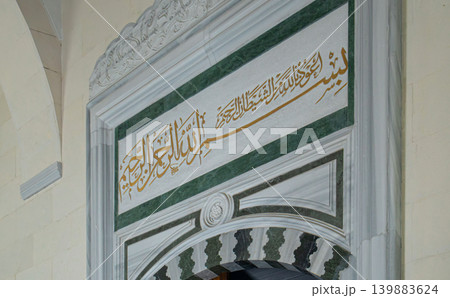 Gold lettering in Arabic hangs on a green marble backdrop above a striped archway in a historic building. The design showcases traditional art in a prominent location. Gold lettering in Arabic hangs on a green marble backdrop above a striped archway in a historic building. The design showcases traditional art in a prominent location. 139883624