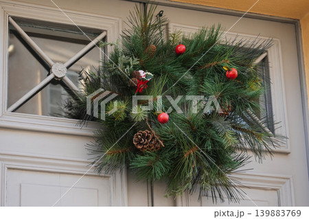 Festive pine wreath with berries hanging on traditional entrance wooden door Festive pine wreath with berries hanging on traditional entrance wooden door 139883769
