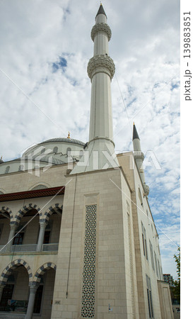 A mosque stands tall with a prominent minaret. Intricate stone patterns cover the exterior. Arched balconies add to the structure's design. Clouds drift above the scene. A mosque stands tall with a prominent minaret. Intricate stone patterns cover the exterior. Arched balconies add to the structure's design. Clouds drift above the scene. 139883851