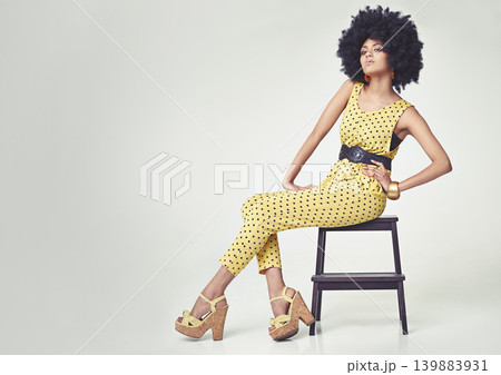 Portrait, fashion and woman with 70s style retro jumpsuit in wedge heels. Sitting on chair with so much confidence, fashionable, elegant female person pretty in yellow dotted outfit, big curly hair Portrait, fashion and woman with 70s style retro jumpsuit in wedge heels. Sitting on chair with so much confidence, fashionable, elegant female person pretty in yellow dotted outfit, big curly hair 139883931