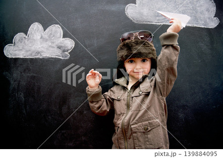 Portrait, chalkboard and toy plane with boy in studio on black background for fantasy game. Children, education and kid pilot in costume playing at school for growth, learning or child development 139884095