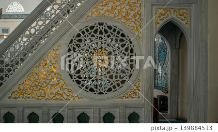 The minbar stands in bright mosque, featuring intricate stone work and gold leaf accents. Traditional star patterns fill the details, reflecting cultural artistry in a sacred space. The minbar stands in bright mosque, featuring intricate stone work and gold leaf accents. Traditional star patterns fill the details, reflecting cultural artistry in a sacred space. 139884513