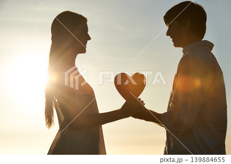 Silhouette, couple and happy with heart shape in nature, commitment and love symbol for marriage by blue sky. Man, woman and valentines day on romantic date and lens flare for bonding on honeymoon Silhouette, couple and happy with heart shape in nature, commitment and love symbol for marriage by blue sky. Man, woman and valentines day on romantic date and lens flare for bonding on honeymoon 139884655