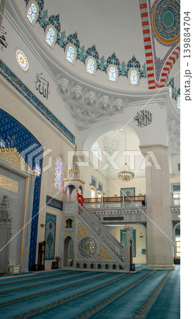The mosque interior shows a marble minbar with golden accents. A Turkish flag is displayed against arched galleries. The space is designed for prayer and reflection. The mosque interior shows a marble minbar with golden accents. A Turkish flag is displayed against arched galleries. The space is designed for prayer and reflection. 139884704