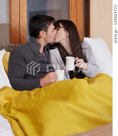 Love, hug and couple kissing on a sofa with trust, support or bonding with coffee and blanket at home. Mouth, embrace or people in living room with security, safety or romance while chilling with tea 139884722