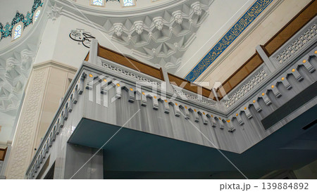The interior of a mosque shows a decorated ceiling and a large chandelier. Light comes through the windows, enhancing the beauty of this space used for prayer and reflection. The interior of a mosque shows a decorated ceiling and a large chandelier. Light comes through the windows, enhancing the beauty of this space used for prayer and reflection. 139884892