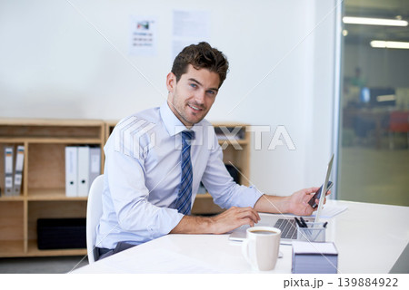 Portrait, desk and businessman with phone, laptop and coffee at startup with technology. Smile, online and business analyst in office with computer, smartphone and internet connection for networking 139884922