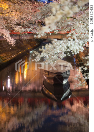 ライトアップされた夜桜と水面に浮かぶ伝統的なたらい舟、奥に佇む赤い橋 139885482