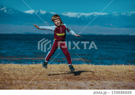 Happy boy jumping on lake background. Issyk-Kul, Kyrgyzstan Happy boy jumping on lake background. Issyk-Kul, Kyrgyzstan 139886889