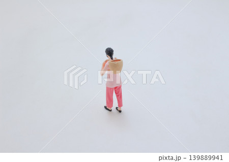 Miniature figure carrying basket on shoulder walking 139889941