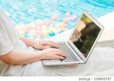 プールサイドのリクライニングチェアに座りパソコンを操作する女性の手元 プールサイドのリクライニングチェアに座りパソコンを操作する女性の手元 139891797