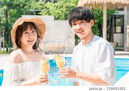 バカンス・リゾートホテルのプールサイドでトロピカルドリンクで乾杯するカップル バカンス・リゾートホテルのプールサイドでトロピカルドリンクで乾杯するカップル 139891802