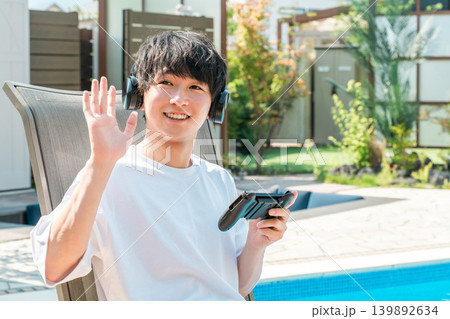 プールサイドでリクライニングチェアに座りゲームをする若いアジア人男性 プールサイドでリクライニングチェアに座りゲームをする若いアジア人男性 139892634