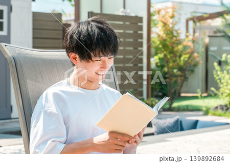 プールサイドでリクライニングチェアに座り読書する若いアジア人男性 プールサイドでリクライニングチェアに座り読書する若いアジア人男性 139892684