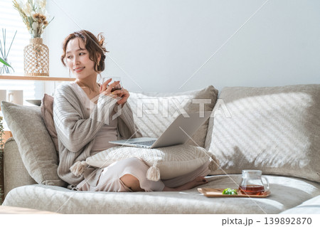 ソファーに座り紅茶を飲みながらパソコンを見る女性 ソファーに座り紅茶を飲みながらパソコンを見る女性 139892870
