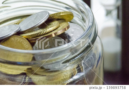 Coins stored in and around an open glass jar Coins stored in and around an open glass jar 139893758