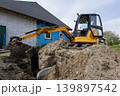 A digger is at work digging a hole beside a structure. The site shows signs of construction with dirt and machinery present on a clear day 139897542