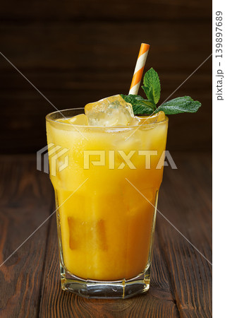 Orange juice in glass with ice cubes, fresh mint sprigs and striped straw on dark wooden surface Orange juice in glass with ice cubes, fresh mint sprigs and striped straw on dark wooden surface 139897689