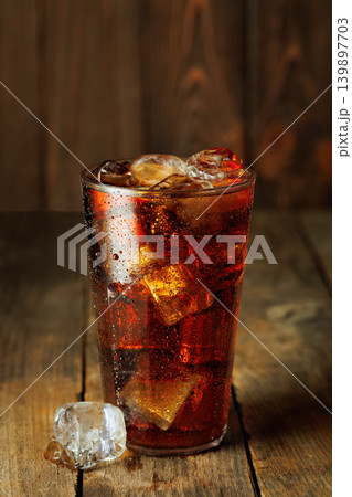 Refreshing sparkling cola with melting ice cubes in a glass creating condensation on rustic wooden background 139897703