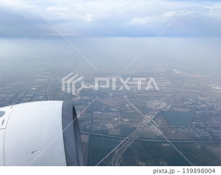 離陸直後の機内から撮影された町並みと水平線まで広がる海と雲 離陸直後の機内から撮影された町並みと水平線まで広がる海と雲 139898004