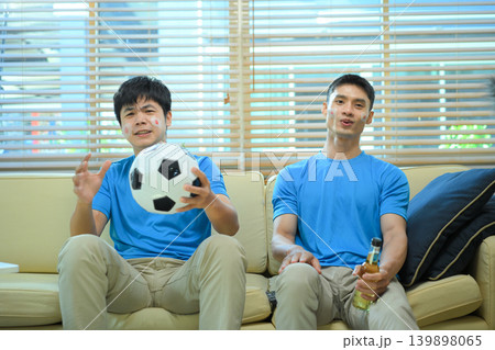 Friends watching soccer game at home, Two men react to match on sofa Friends watching soccer game at home, Two men react to match on sofa 139898065