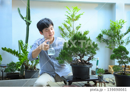 Man watering bonsai tree in calm home garden setting Man watering bonsai tree in calm home garden setting 139898081