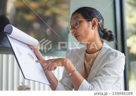 Side view businesswoman pointing to business report charts in office, explaining financial data, marketing analysis, strategy discussion, and confident professional presentation for team meeting. 139898109