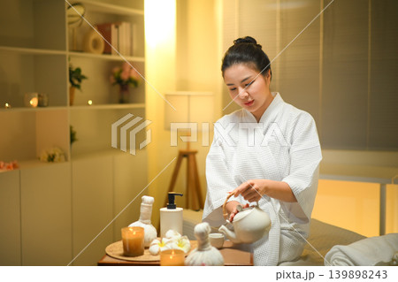 Woman pouring herbal tea in spa setting with warm light and calm wellness mood 139898243