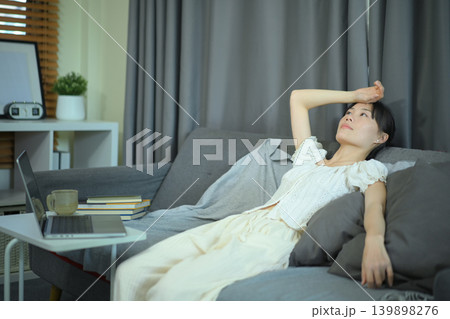Young woman lying on sofa looking concerned beside laptop Young woman lying on sofa looking concerned beside laptop 139898276