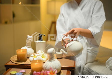 Woman pouring herbal tea in spa setting with warm light and calm wellness mood Woman pouring herbal tea in spa setting with warm light and calm wellness mood 139898278