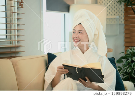 Young woman in bathrobe reads book on sofa Young woman in bathrobe reads book on sofa 139898279