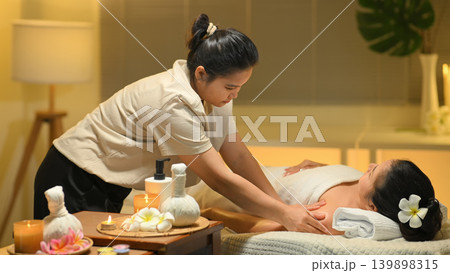 Therapist massaging shoulder of woman at spa with warm light calm wellness scene 139898315