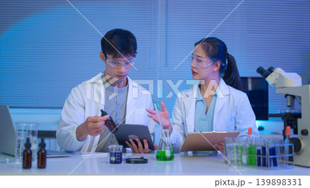 Two scientists discuss and record experimental data using tablet and clipboard in a modern laboratory with liquid samples and equipment 139898331